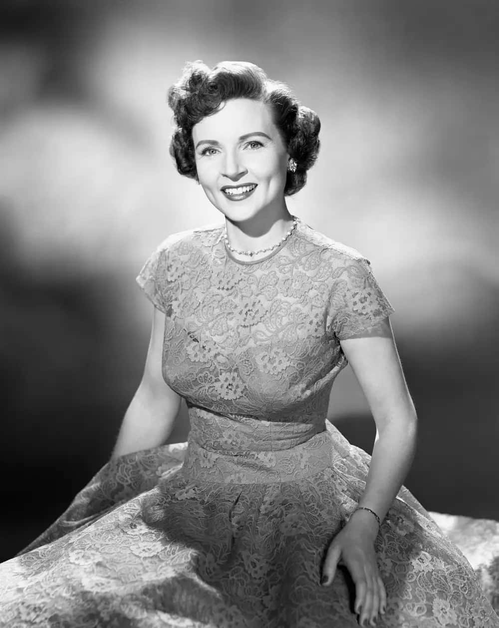A Woman In A Dress Is Smiling In A Black And White Photo