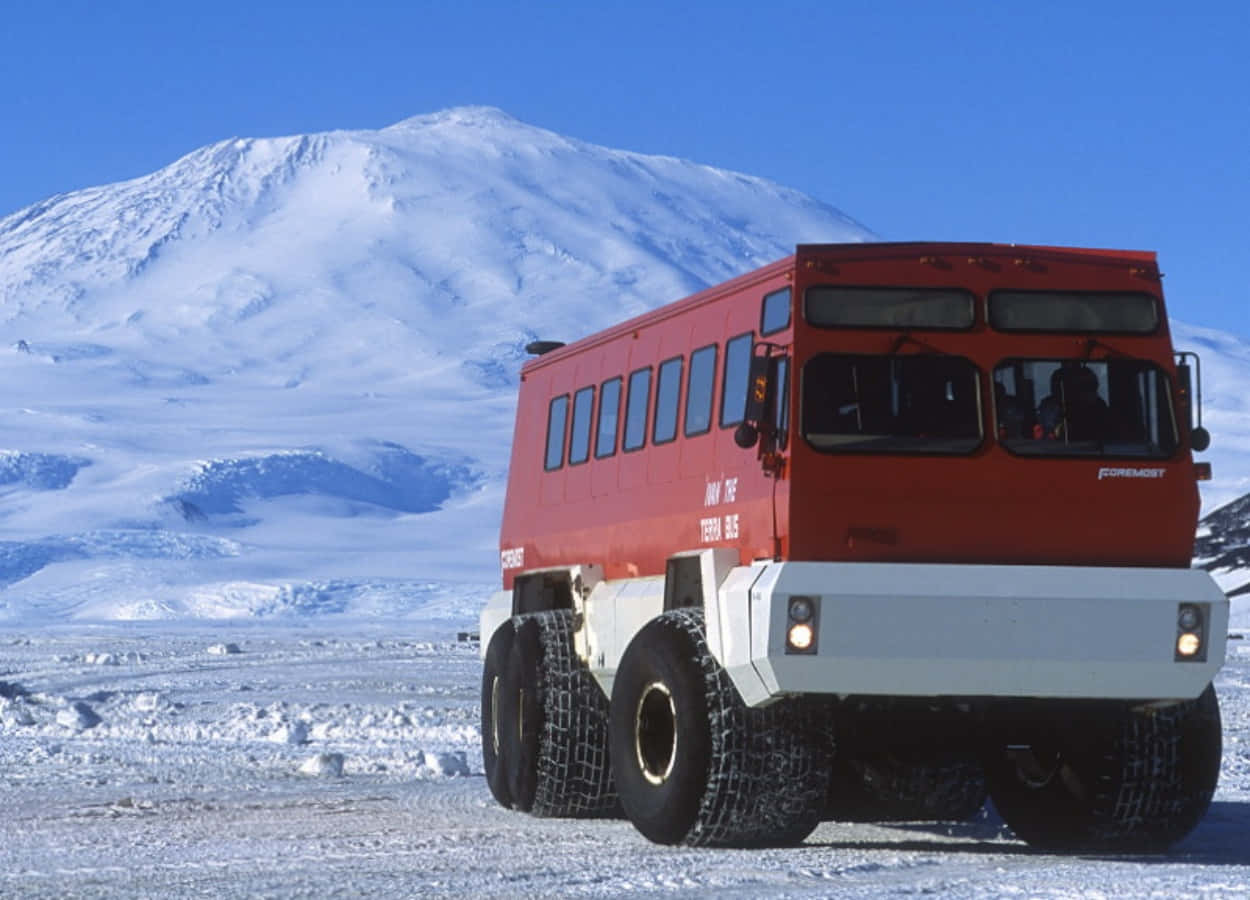 A Red Truck Driving On A Snowy Road With A Mountain In The Background