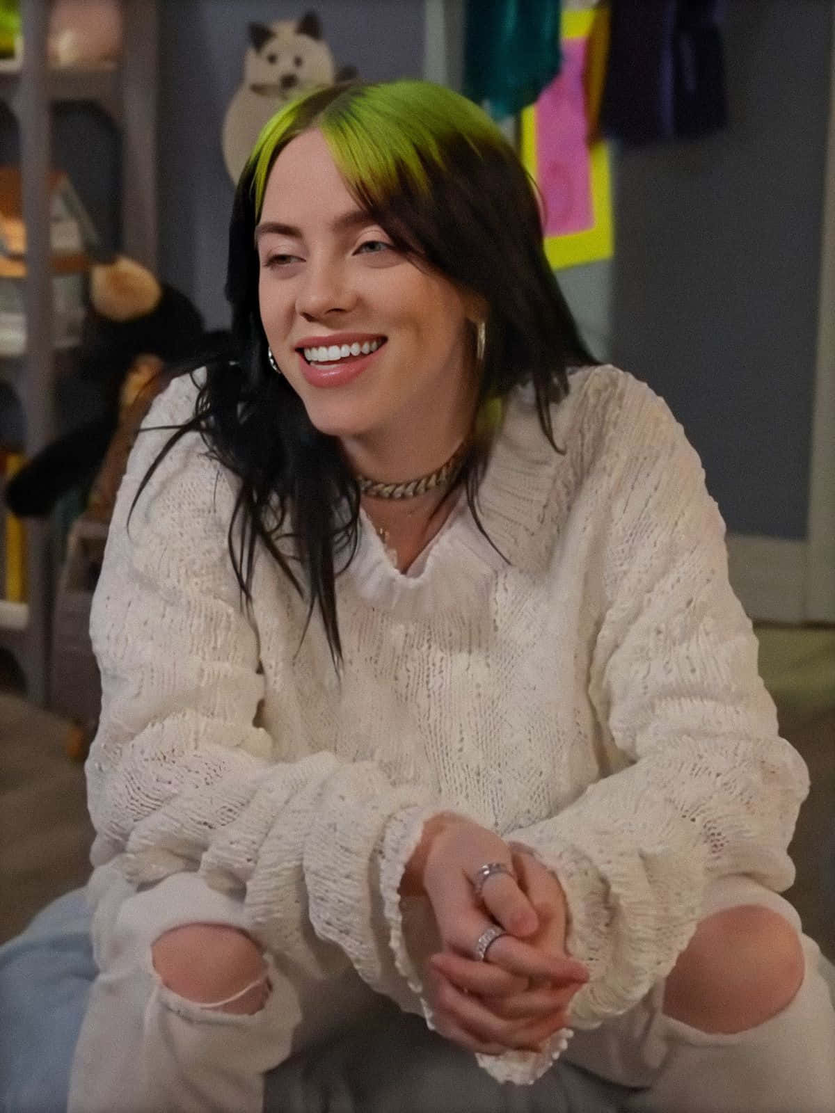 Billie Eilish wearing her signature green hoodie and smiling. Wallpaper
