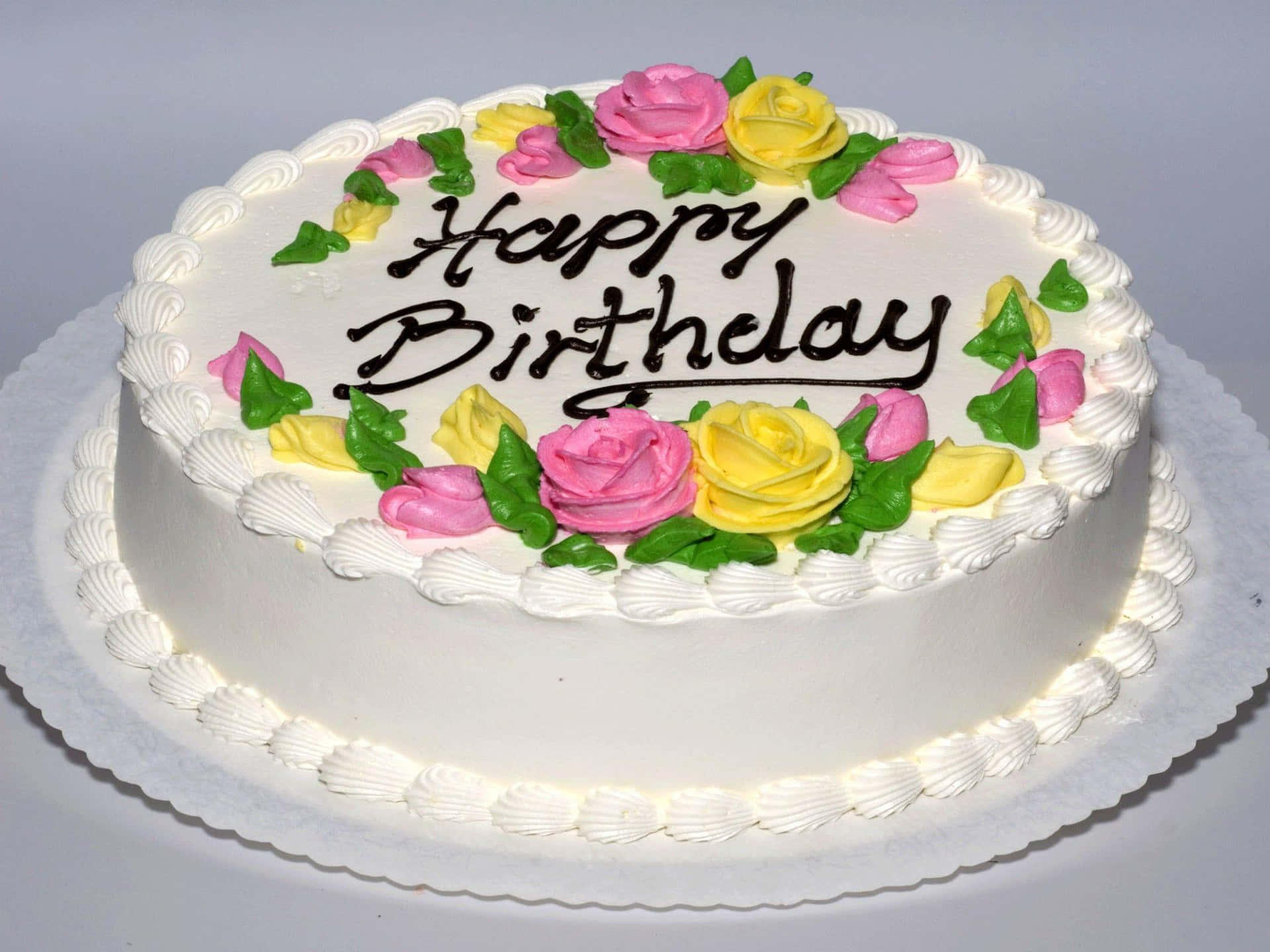 En hvid kage med blomster på den er dekoreret med glade fødselsdagsmærkater