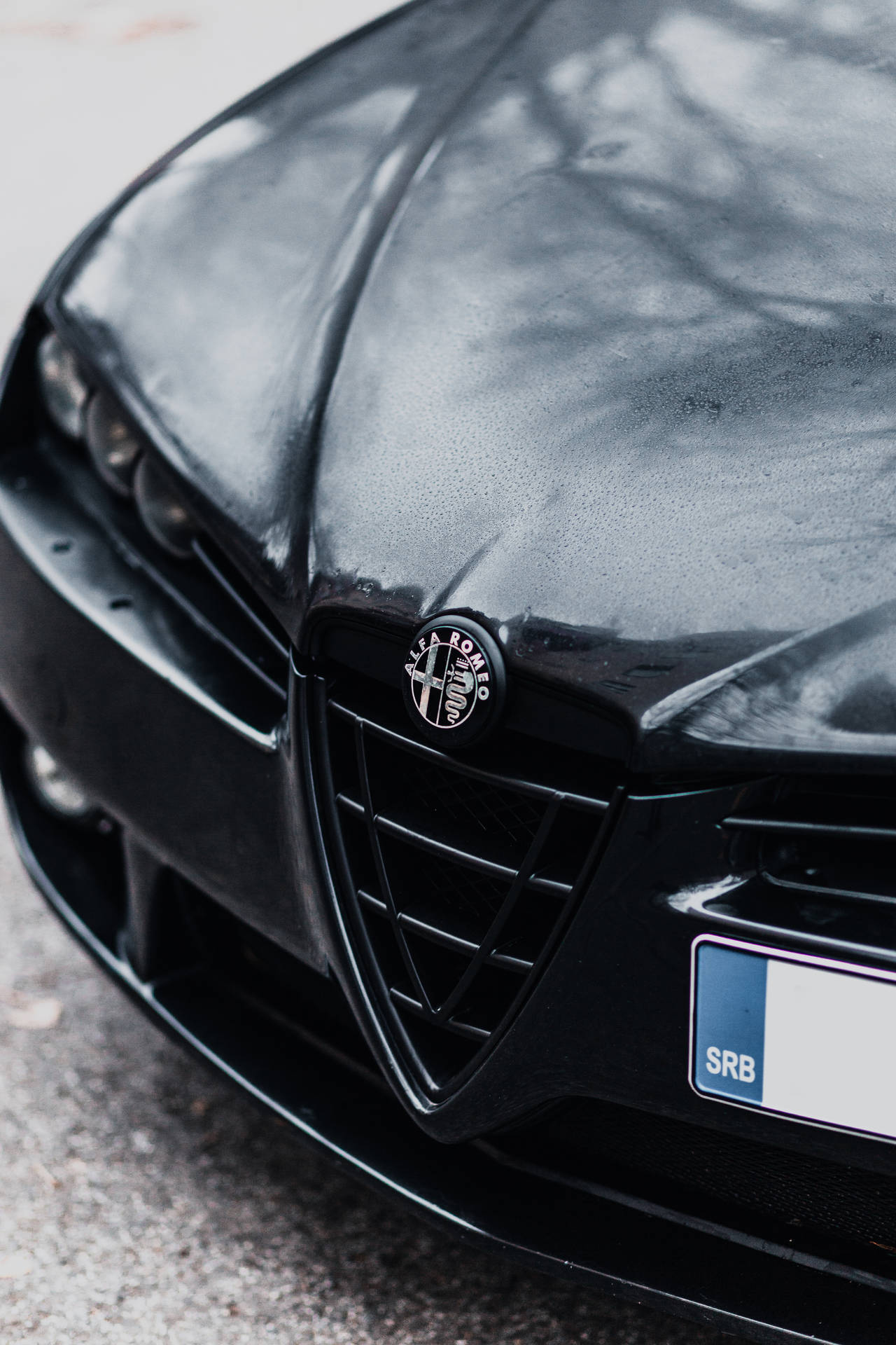 Black Alfa Romeo close-up with red cross and biscione snake logo wallpaper.