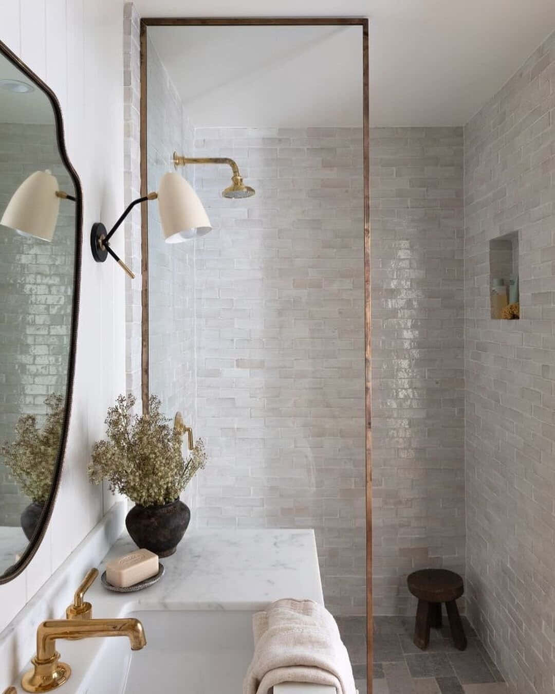 A Bathroom With A White Tiled Shower And Brass Fixtures