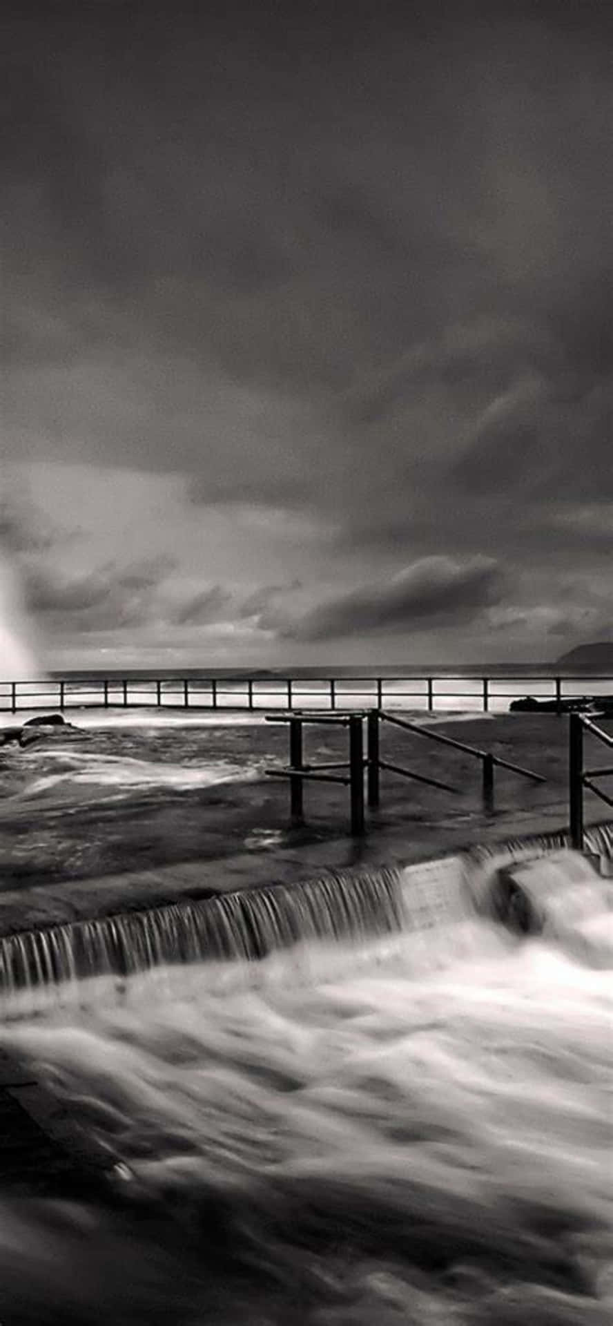 A Black And White Photo Of A Pier With Waves