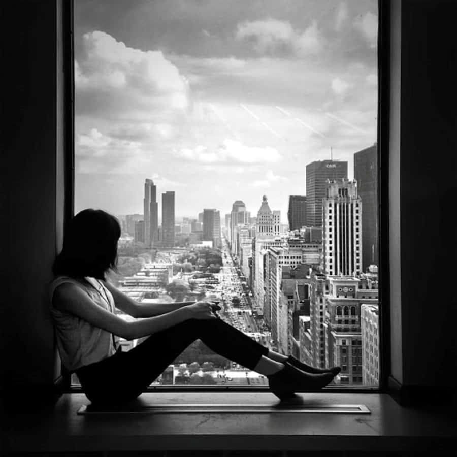 a woman sitting on a window sill looking out at the city