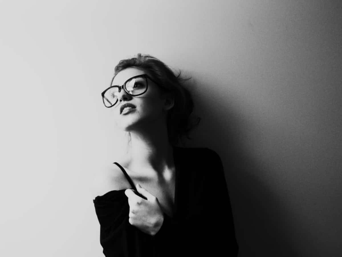 a woman in glasses is posing against a wall