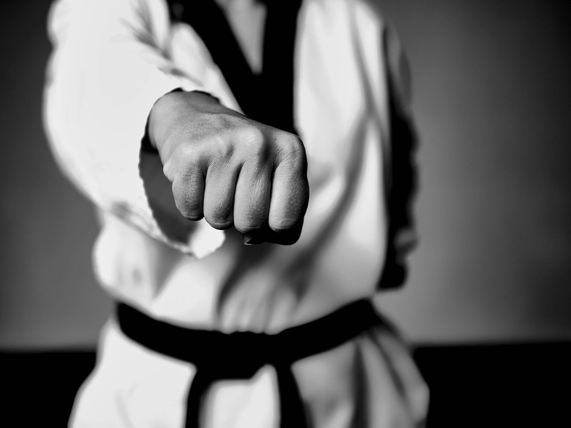 Taekwondo practitioner demonstrating a front hand middle punch in black and white Wallpaper