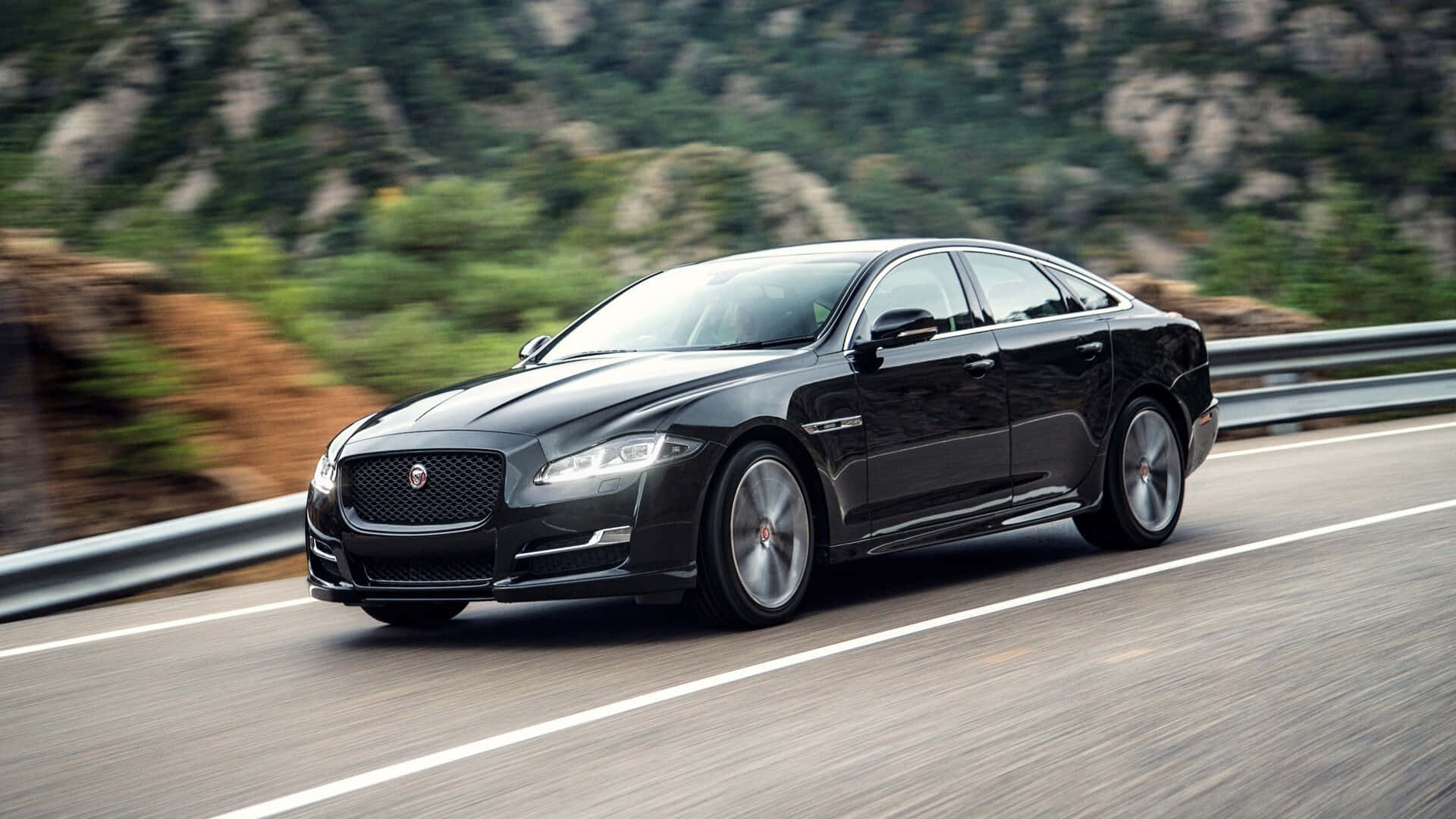The Black Jaguar Xf Is Driving Down A Mountain Road