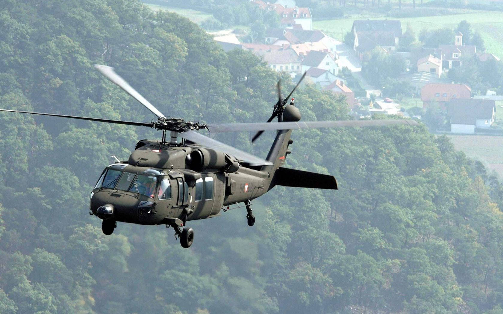 Unhelicóptero Negro Volando Sobre Un Bosque Fondo de pantalla