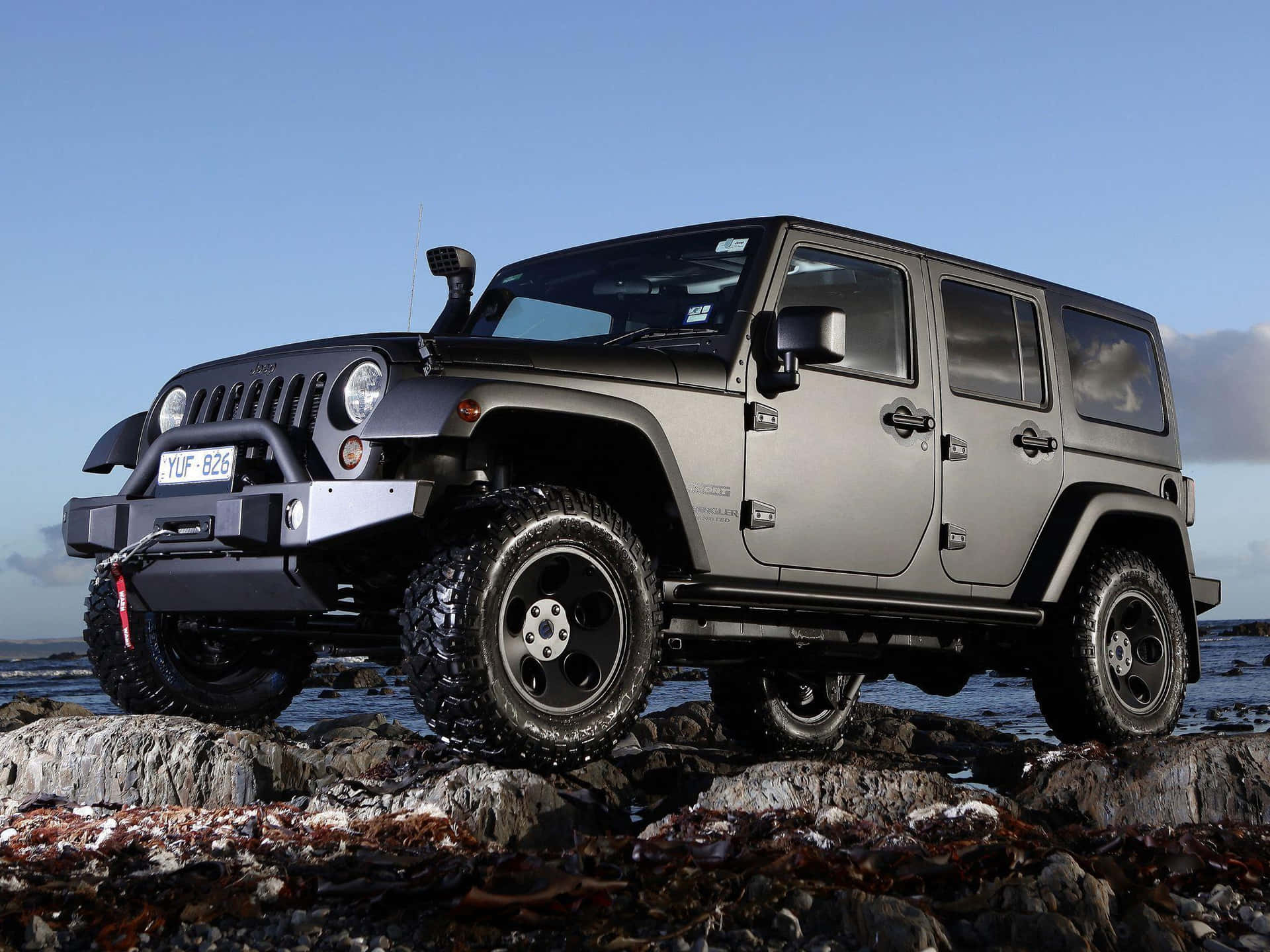 A Black Jeep Is Parked On Rocks Near The Ocean