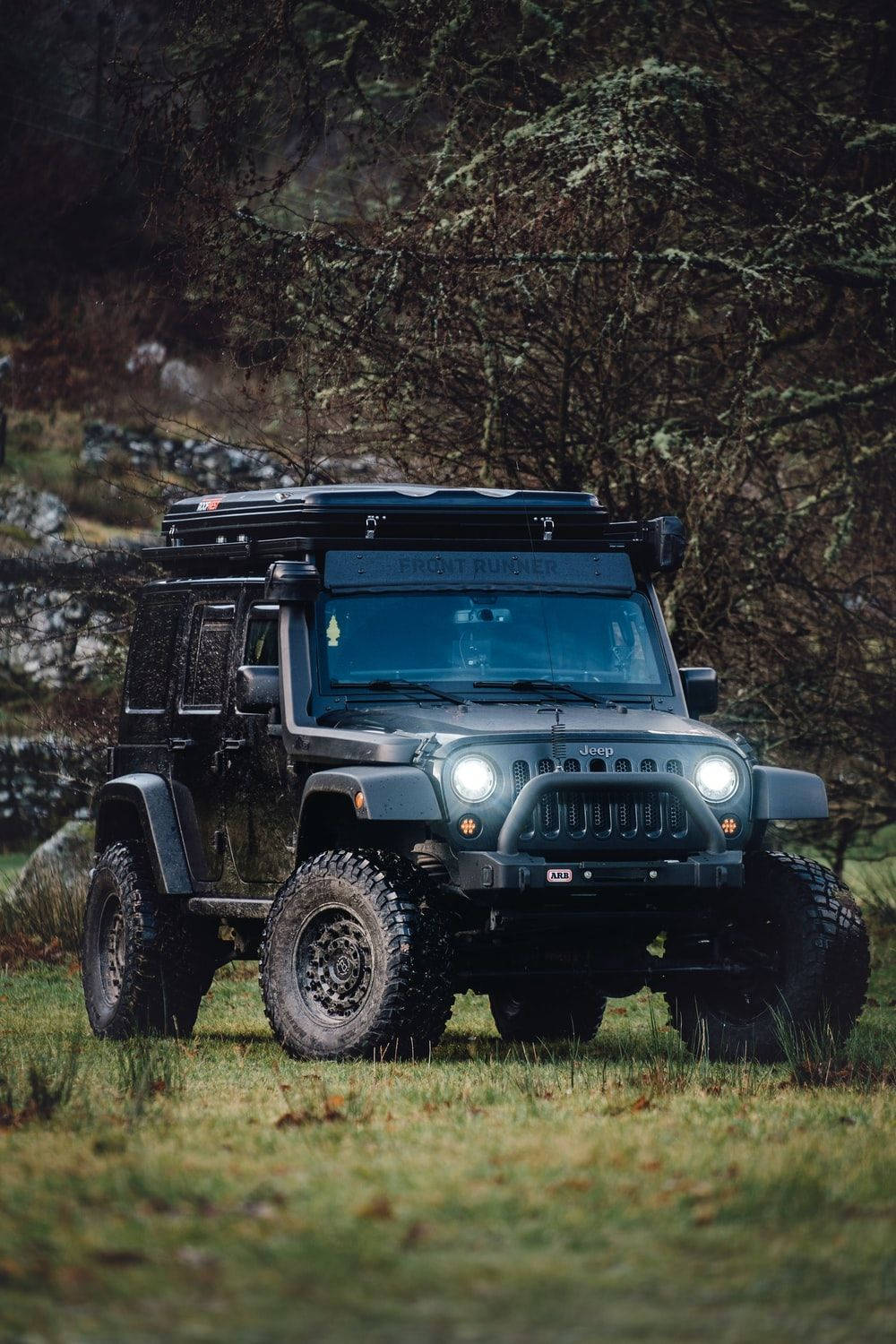 Dynamic Black Jeep Wrangler with Top Rack Over Rugged Terrain Wallpaper
