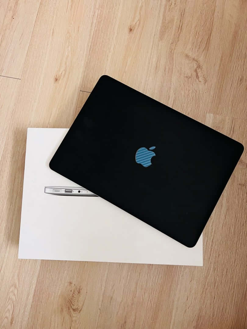 A sleek black Macbook sitting on a white desk Wallpaper