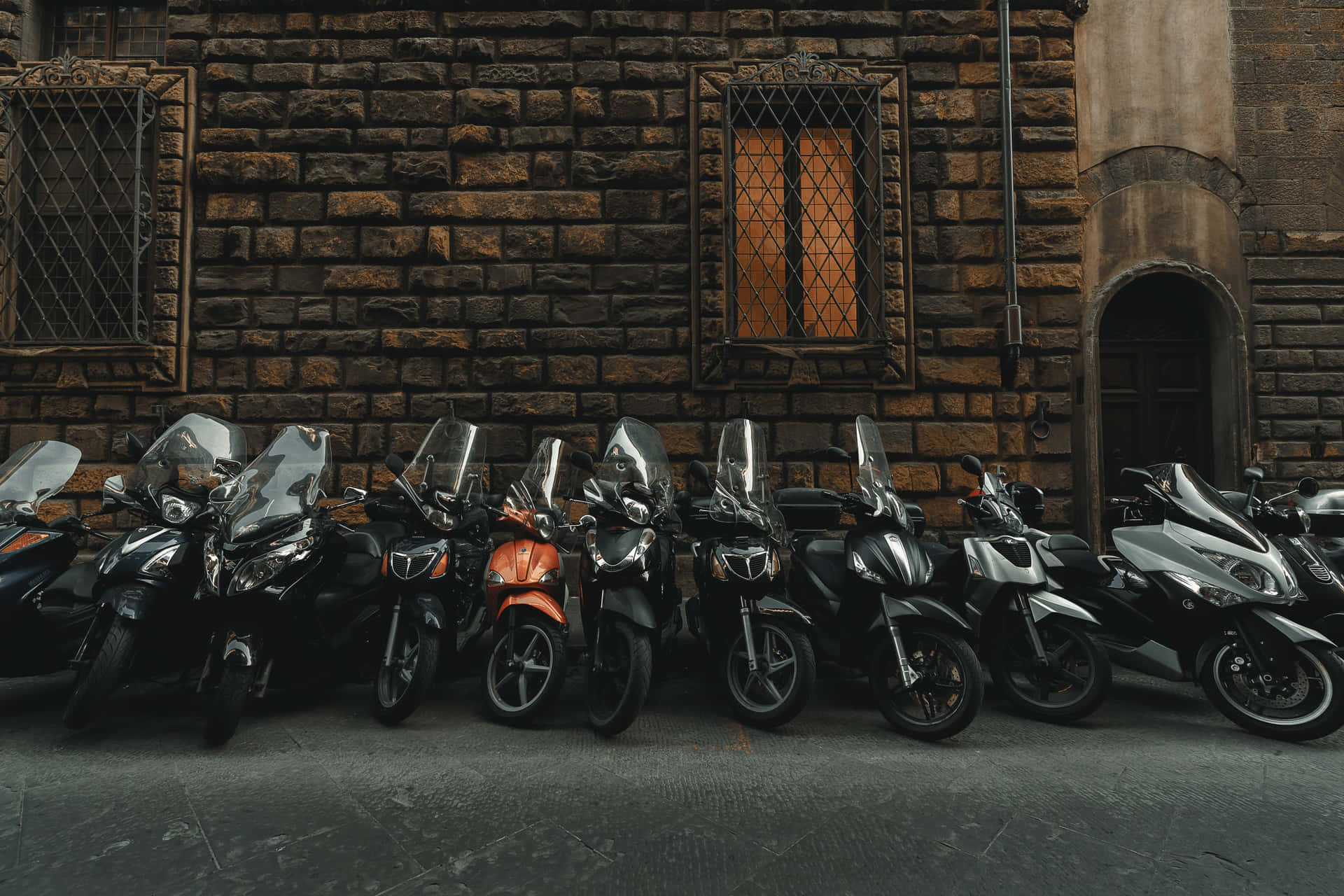 Black Motorcycles Lining Up With A Conspicuous Orange One Wallpaper