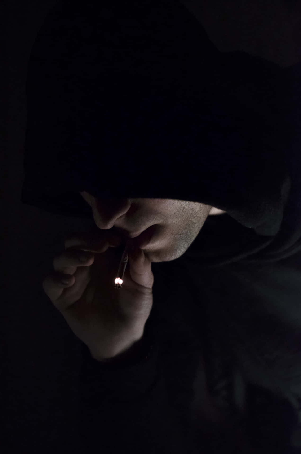 A Man In A Hoodie Smoking A Cigarette In The Dark