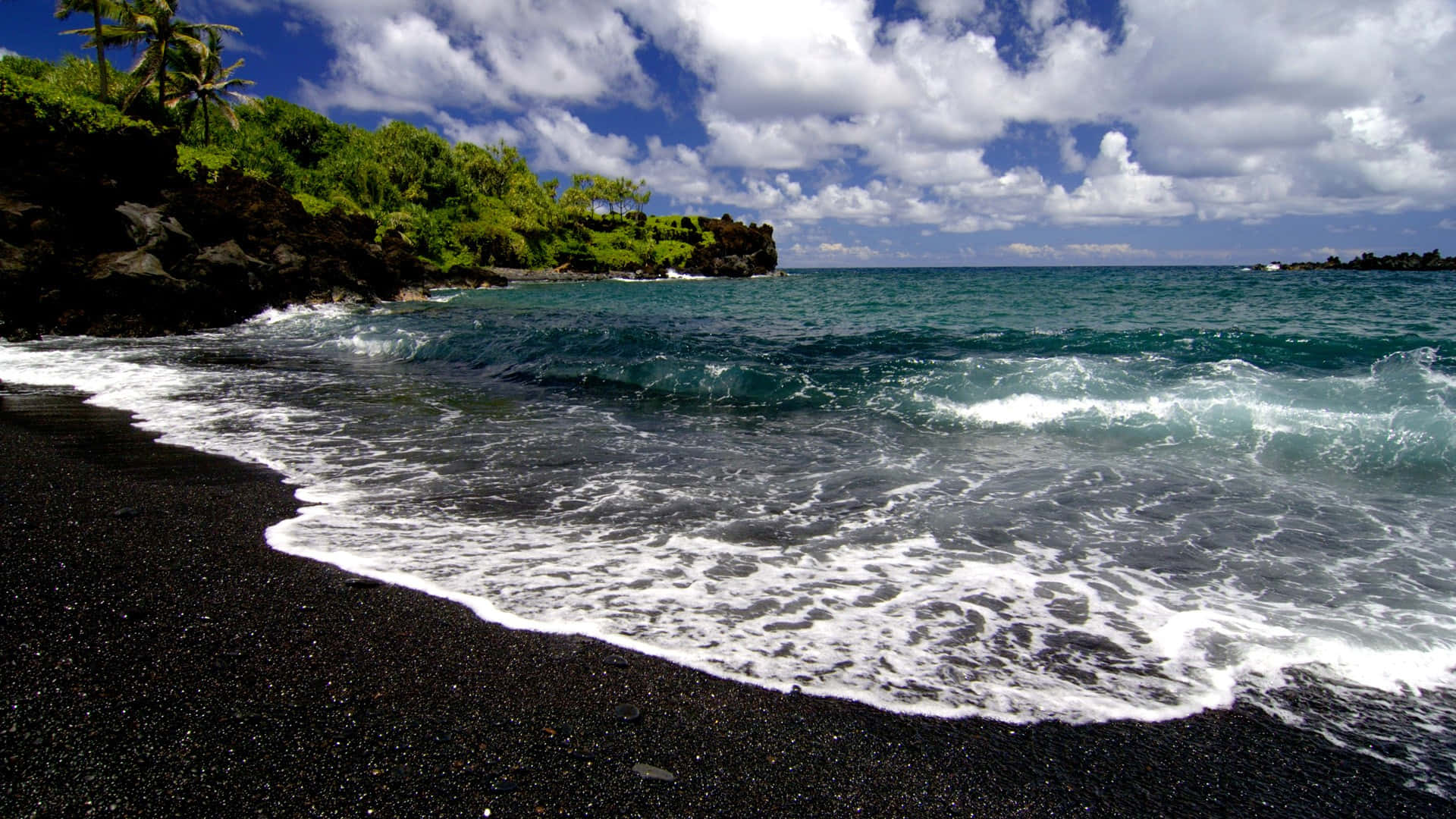 A tranquil black sand beach with inviting blue ocean waters Wallpaper