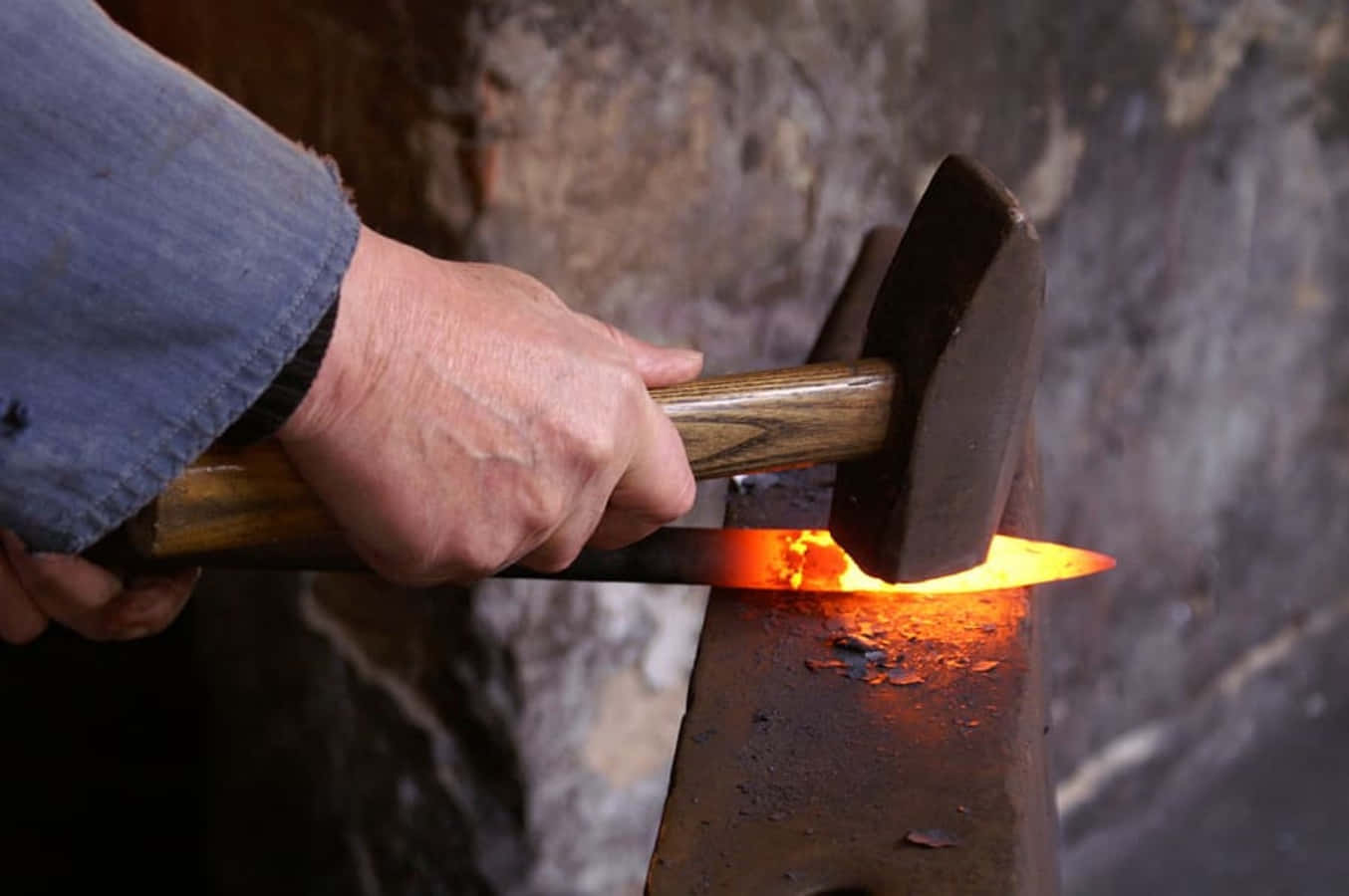 An old-time blacksmith works away at his anvil Wallpaper