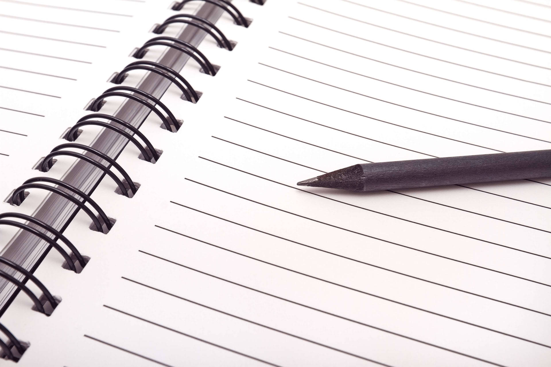 Close-up view of a blank page in a spiral notebook with a pen alongside. Wallpaper
