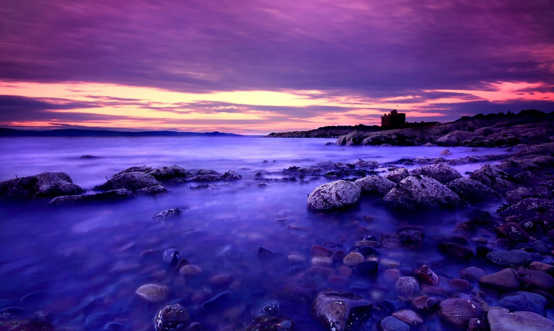 Rocky Shore With A Blue And Purple Sunset Wallpaper