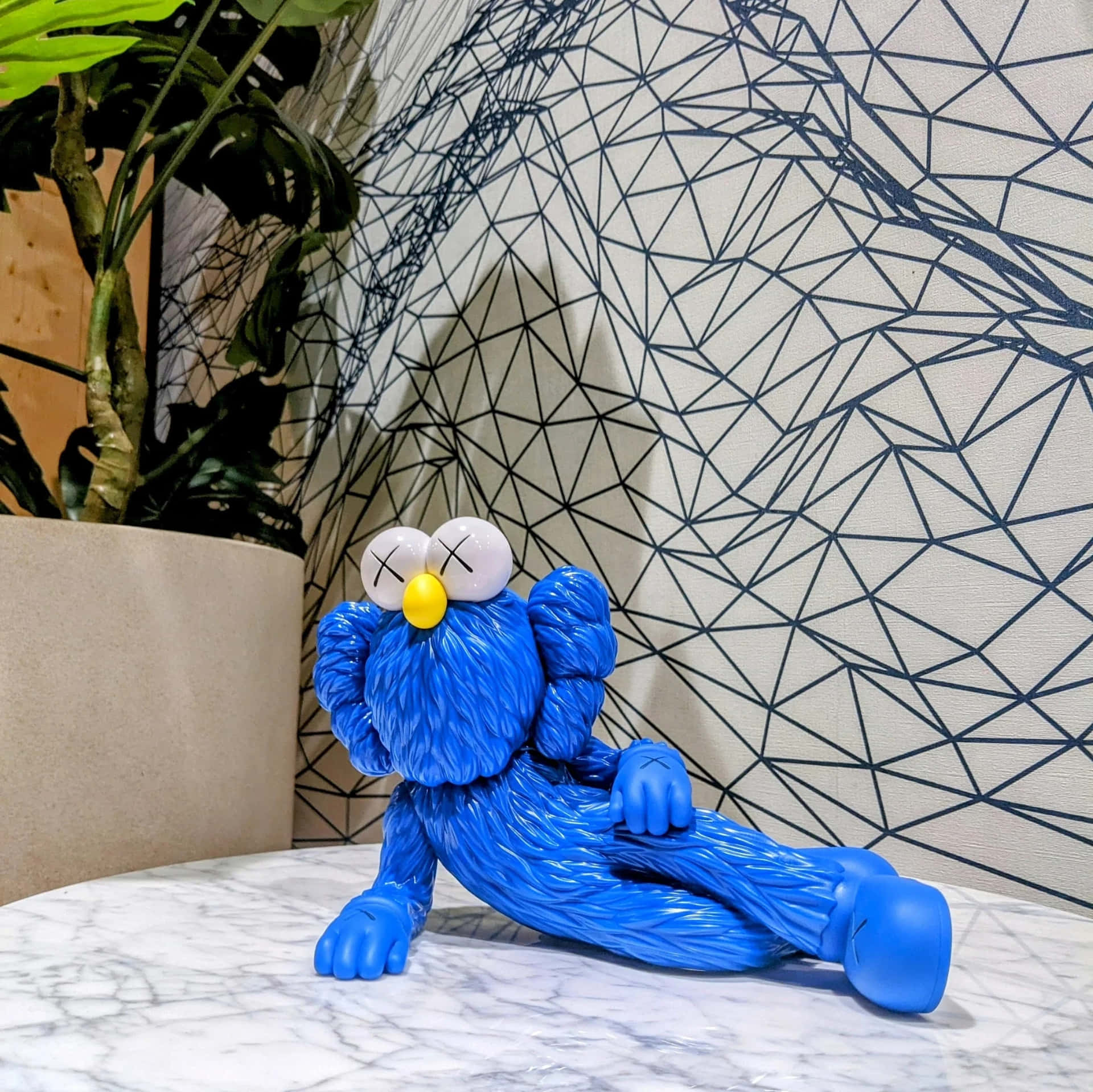 Blue Kaws Figure Relaxing On Table Wallpaper