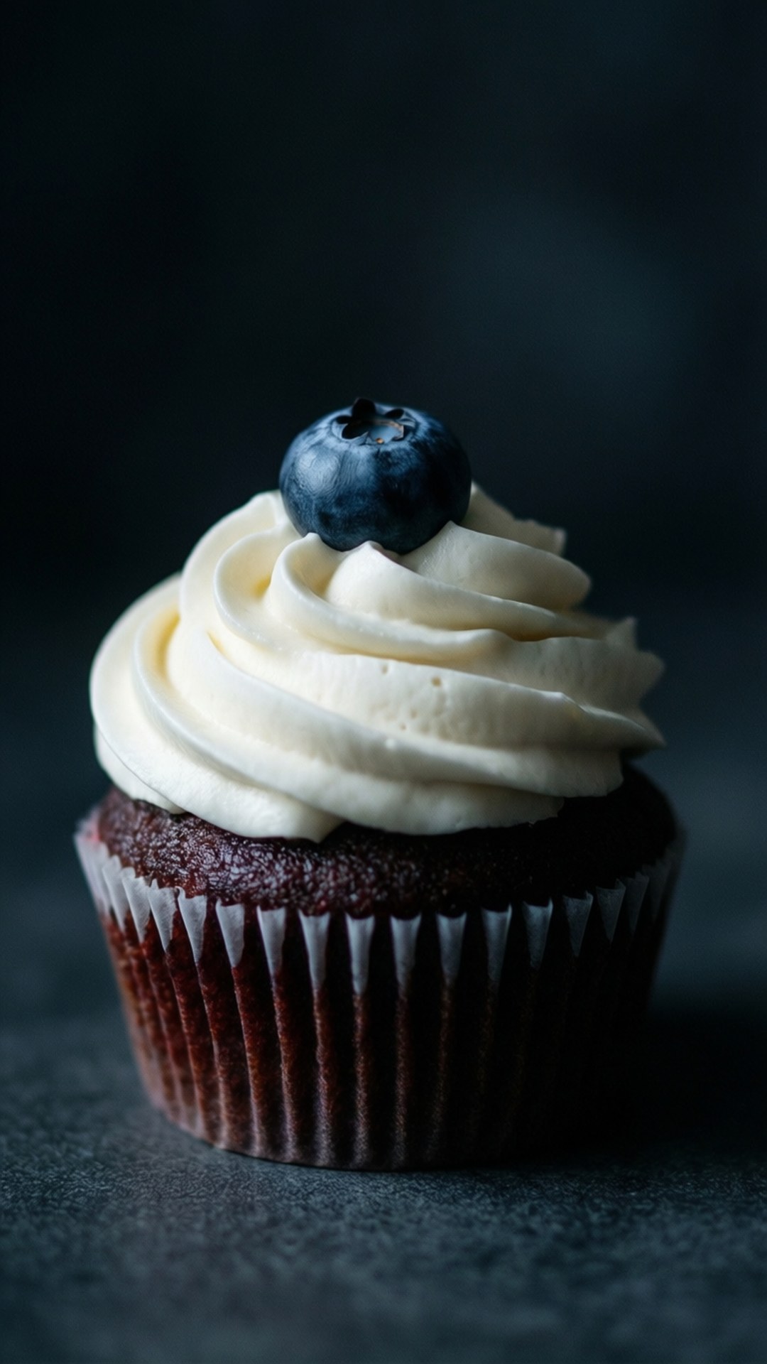 Blueberry cupcake with white frosting in moody lighting.