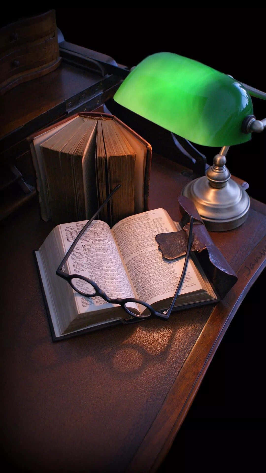 En grøn lampe på et skrivebord med bøger. Wallpaper