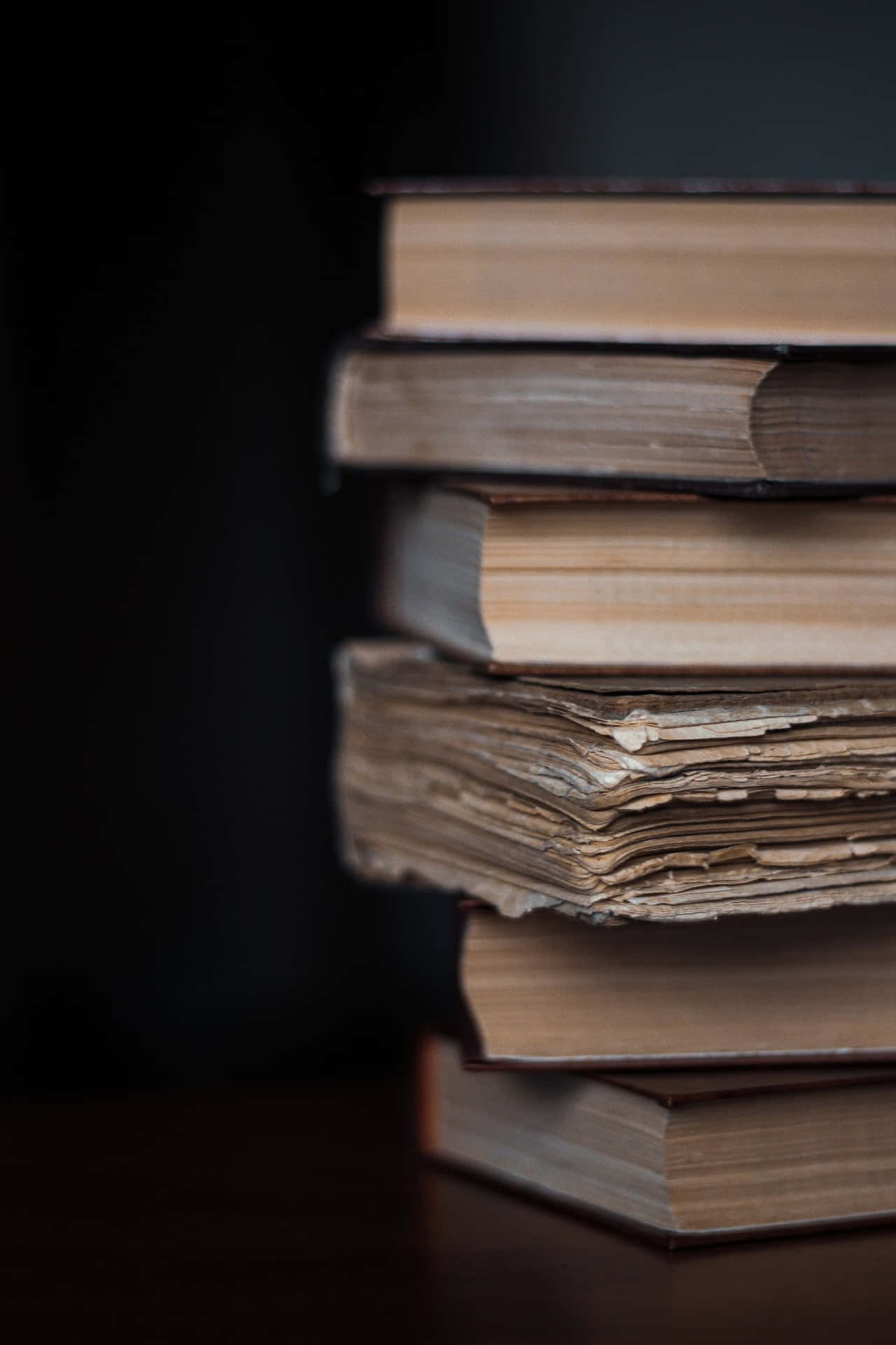A Stack Of Books On A Table With A Dark Background Wallpaper
