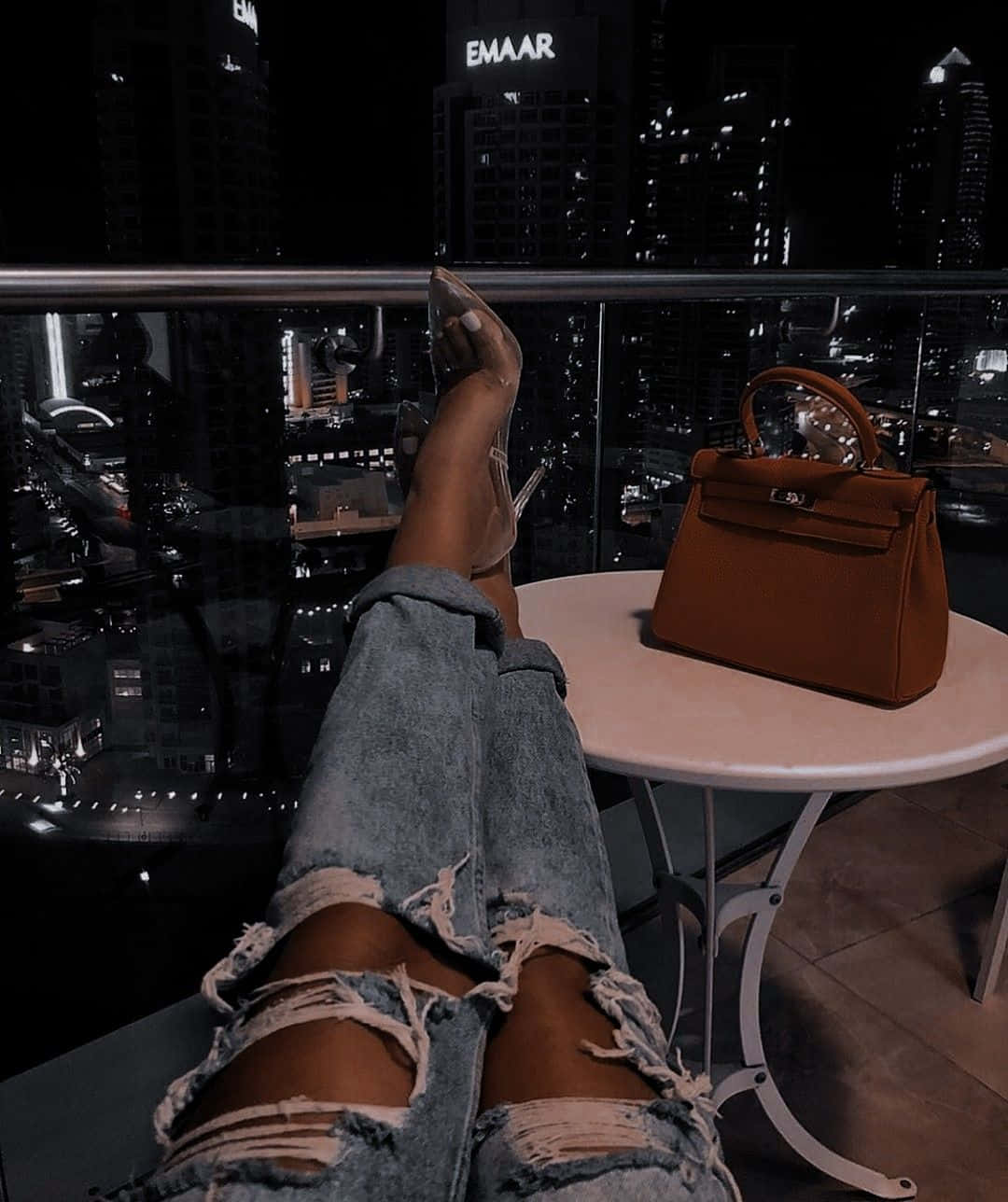 A Woman's Legs On A Table With A Purse And Ripped Jeans Wallpaper