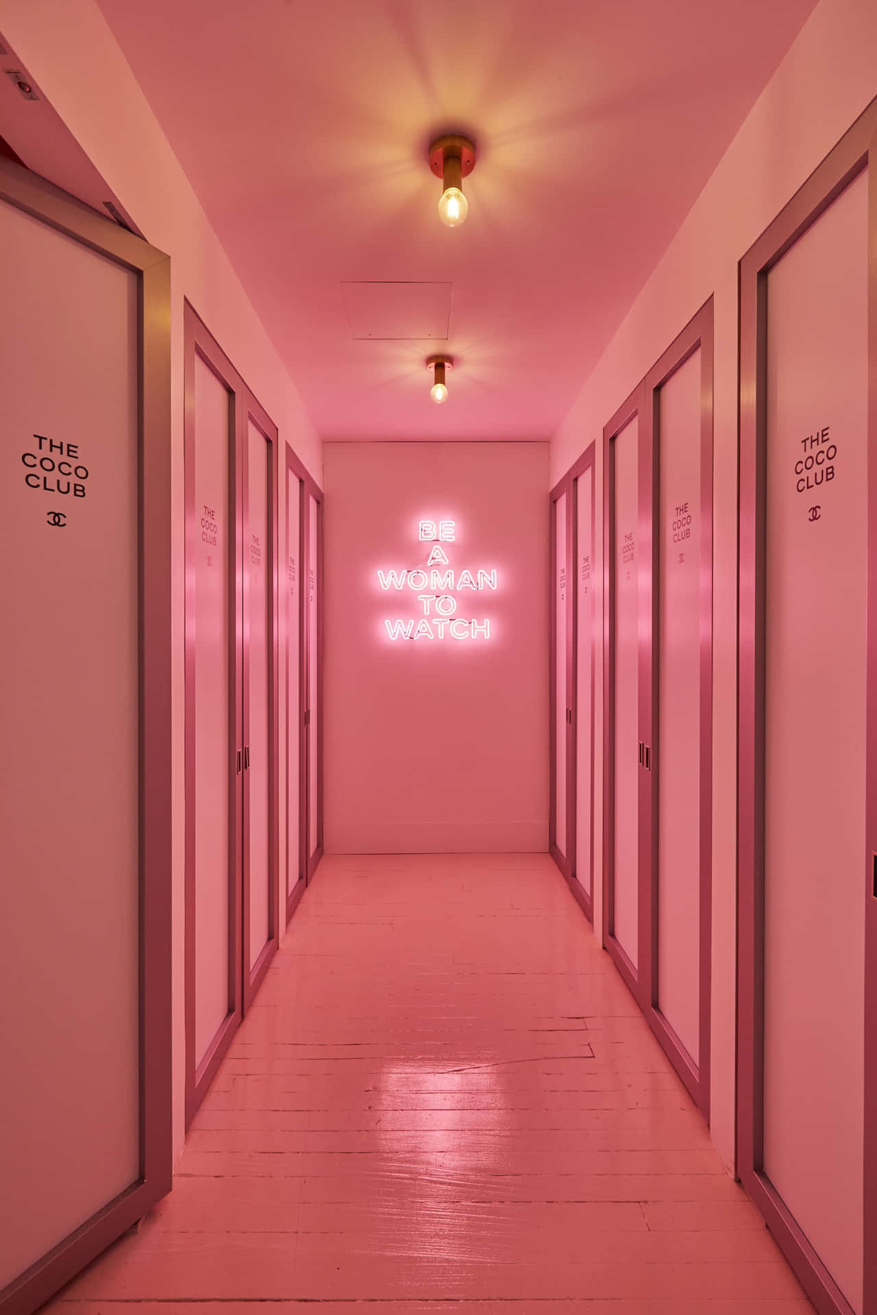 A Hallway With Pink Doors And A Neon Sign Wallpaper