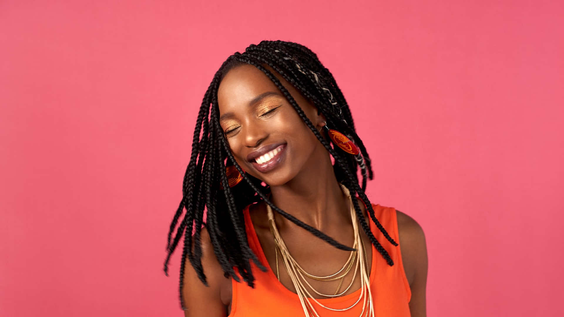 A Young Woman With Braids Smiling On A Pink Background