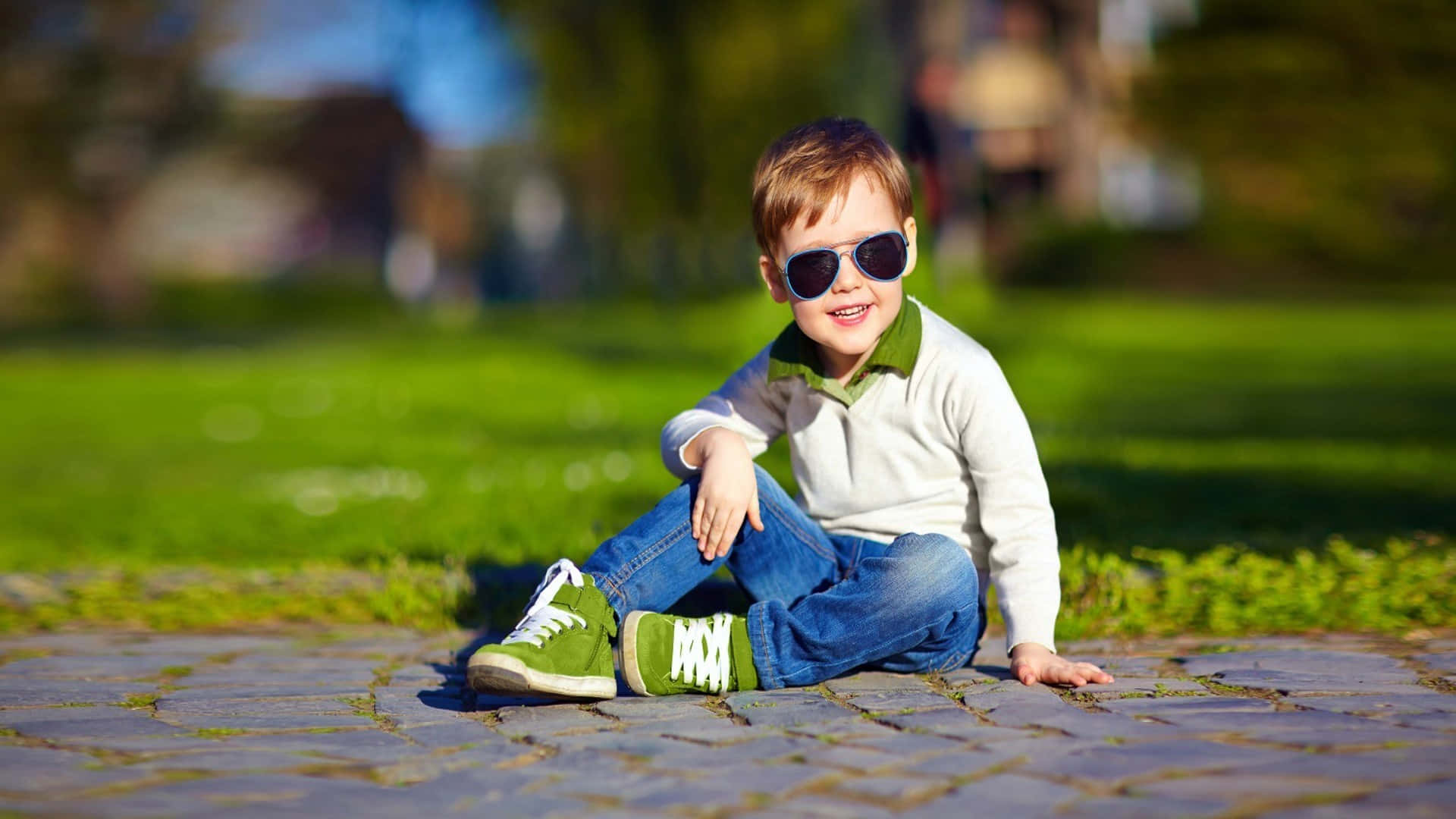 A Young Boy Wearing Sunglasses Sitting On The Ground