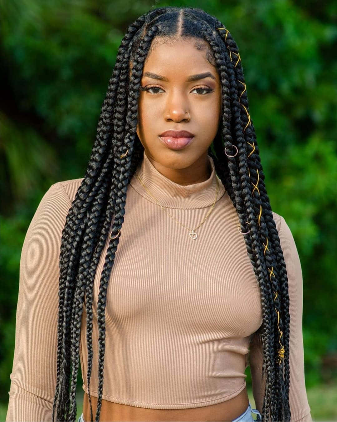 A Young Black Woman Wearing A Beige Top And Long Braids