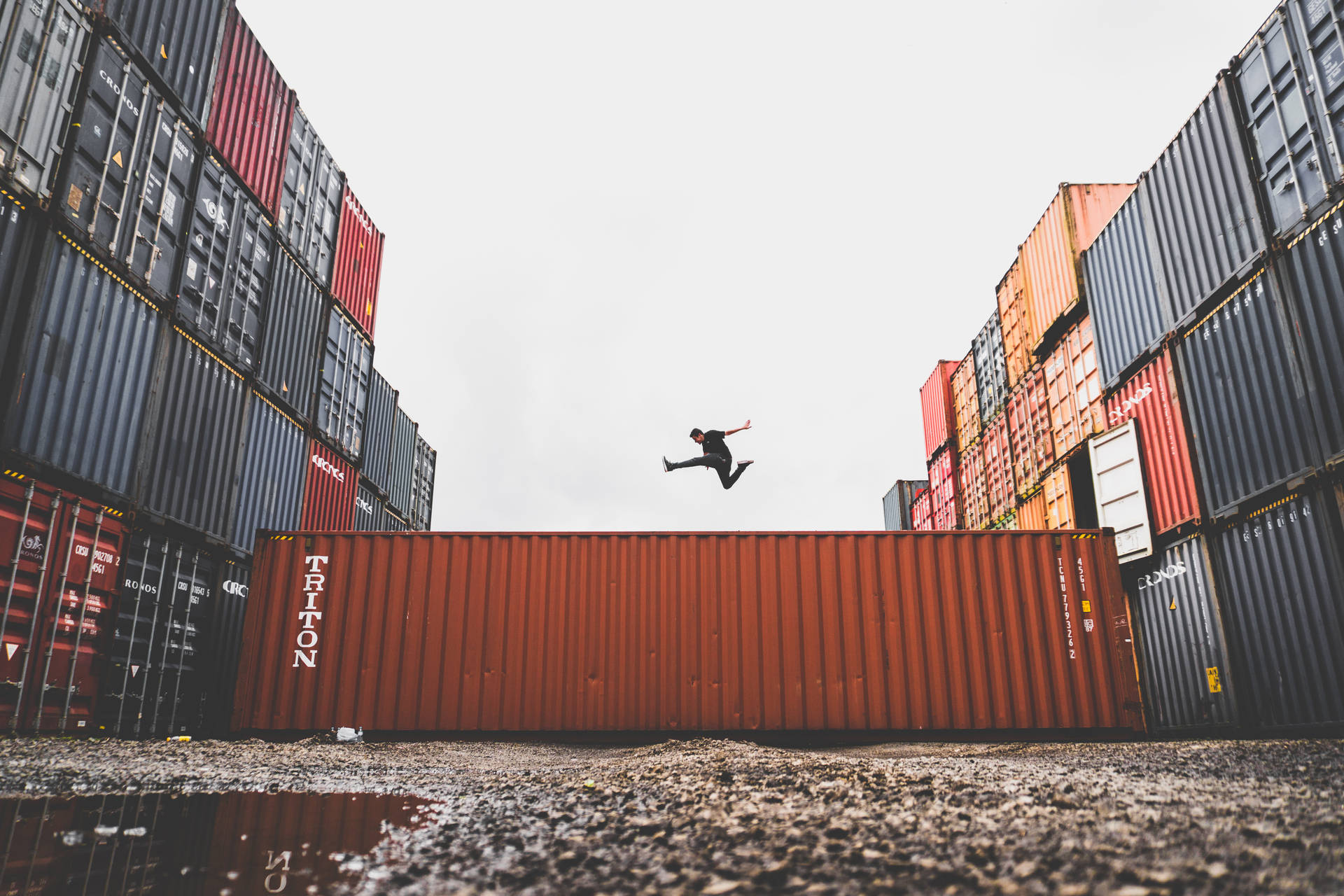 Caption: Fearless Leap Amidst Shipping Containers Wallpaper