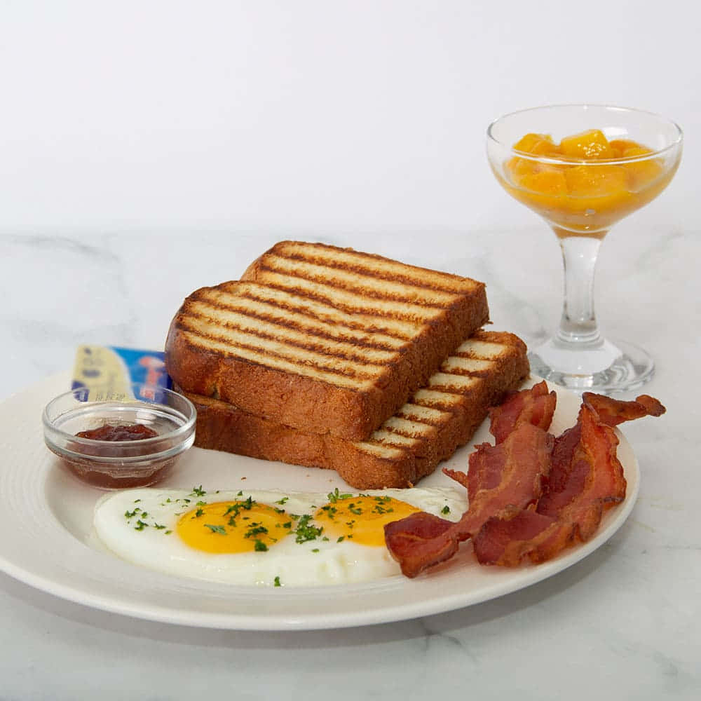 A Plate With A Breakfast Sandwich, Eggs, Bacon And Fruit