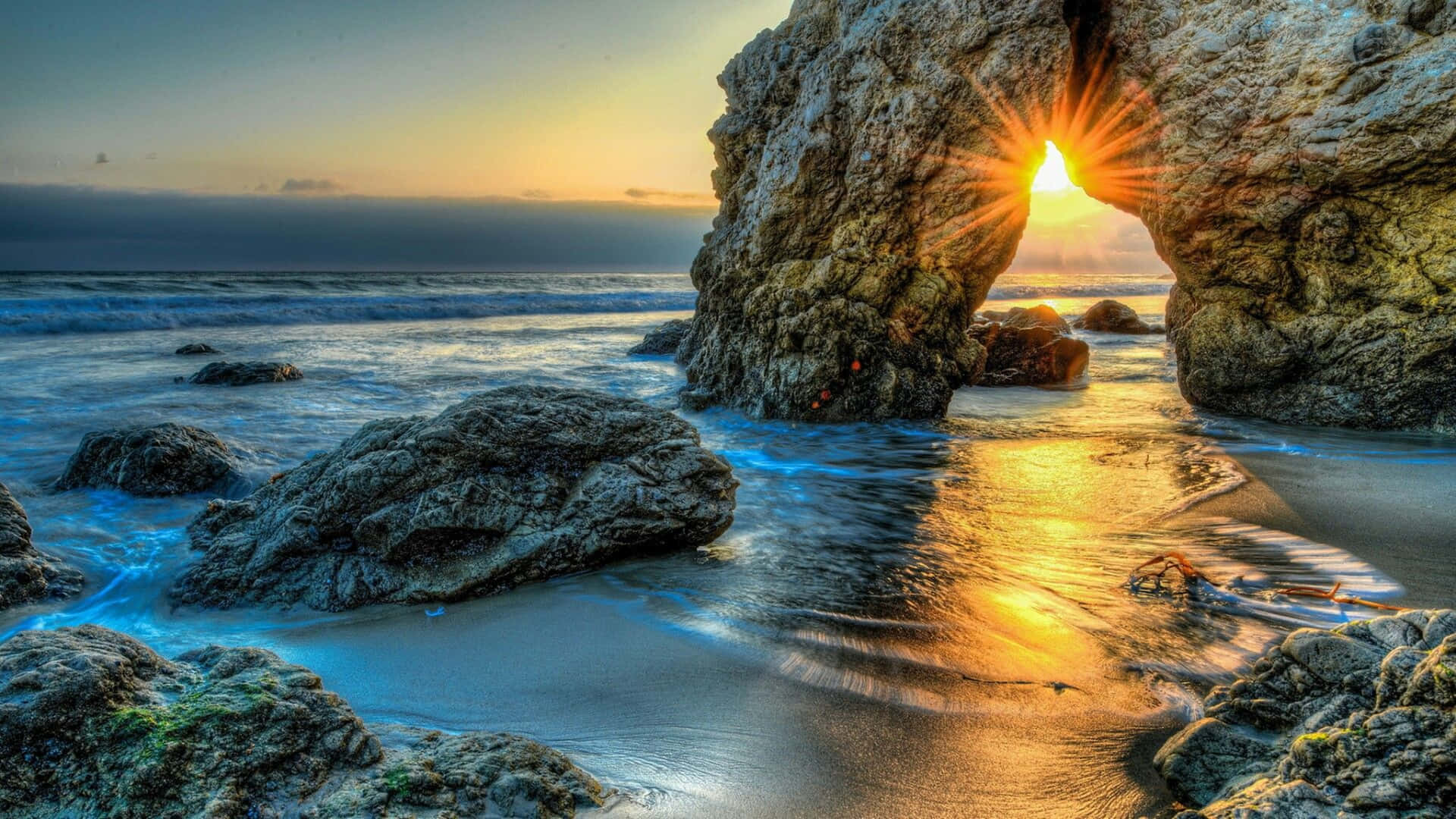 A Rock Arch In The Ocean At Sunset Wallpaper
