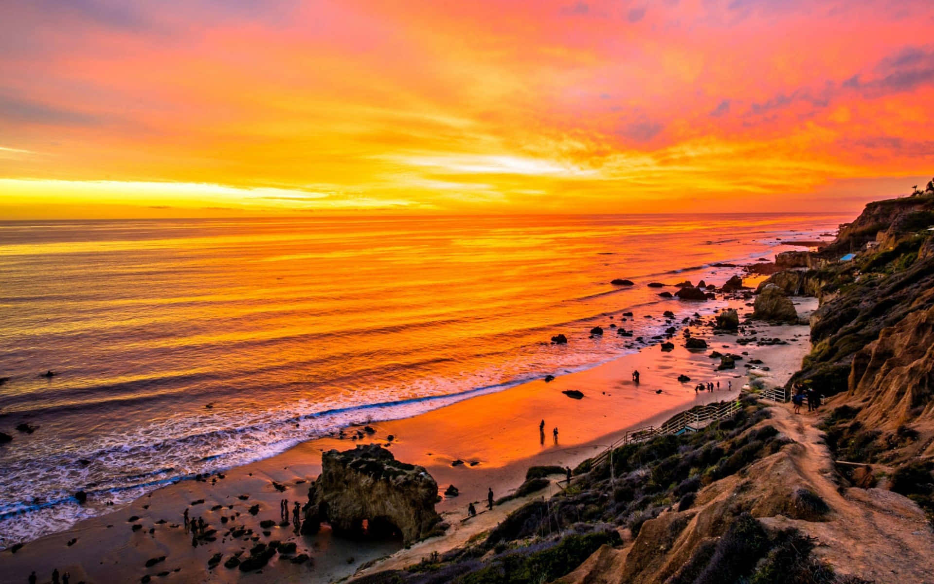 A Sunset Over A Beach With People On The Cliffs Wallpaper