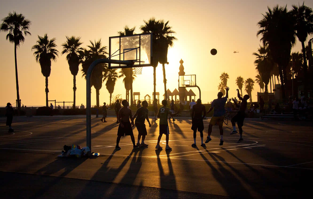 Einegruppe Von Menschen Spielt Basketball Bei Sonnenuntergang. Wallpaper