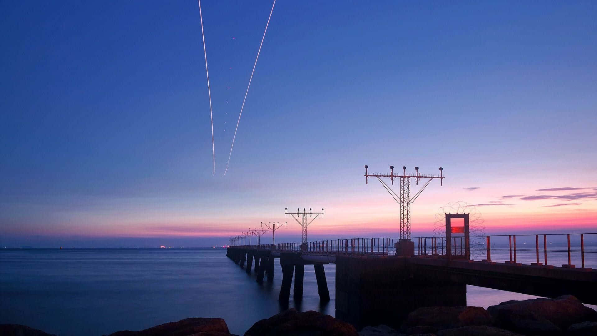 A Plane Flying Over A Pier At Sunset Wallpaper