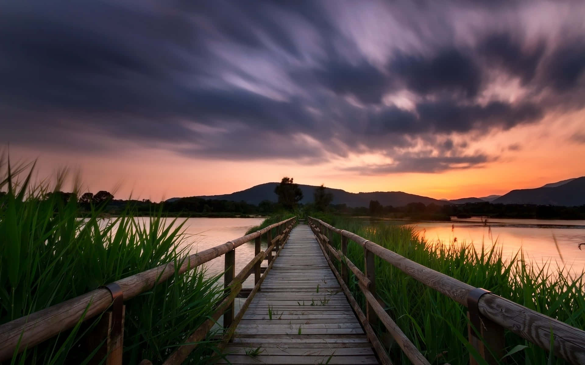 a wooden bridge leading to a lake at sunset