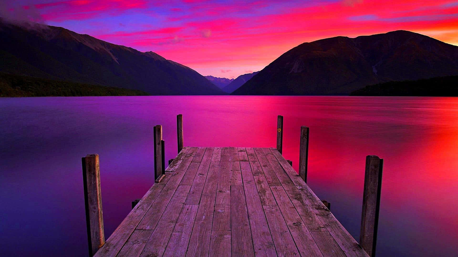 A Dock With A Colorful Sunset Over A Lake