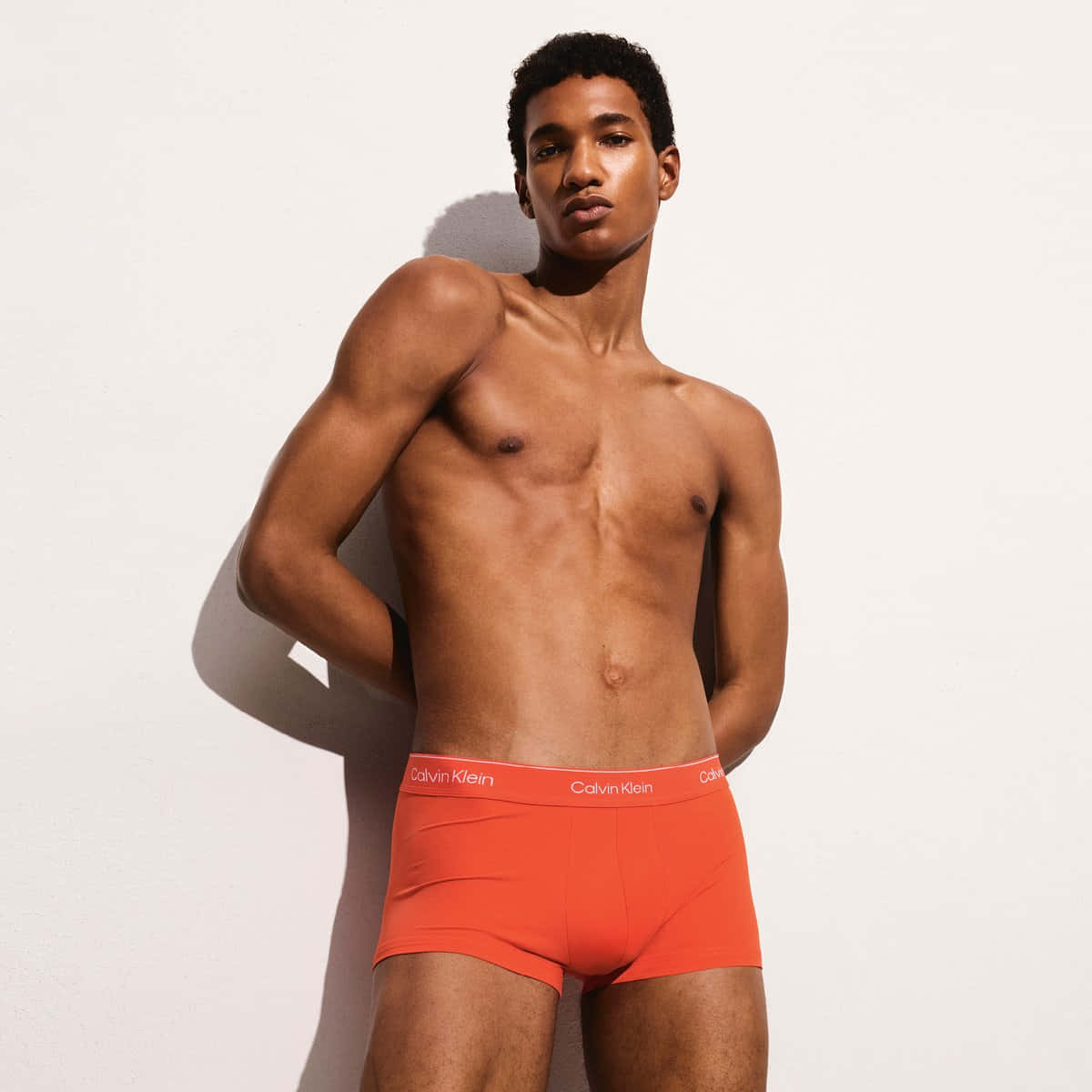 a man in orange trunks leaning against a wall