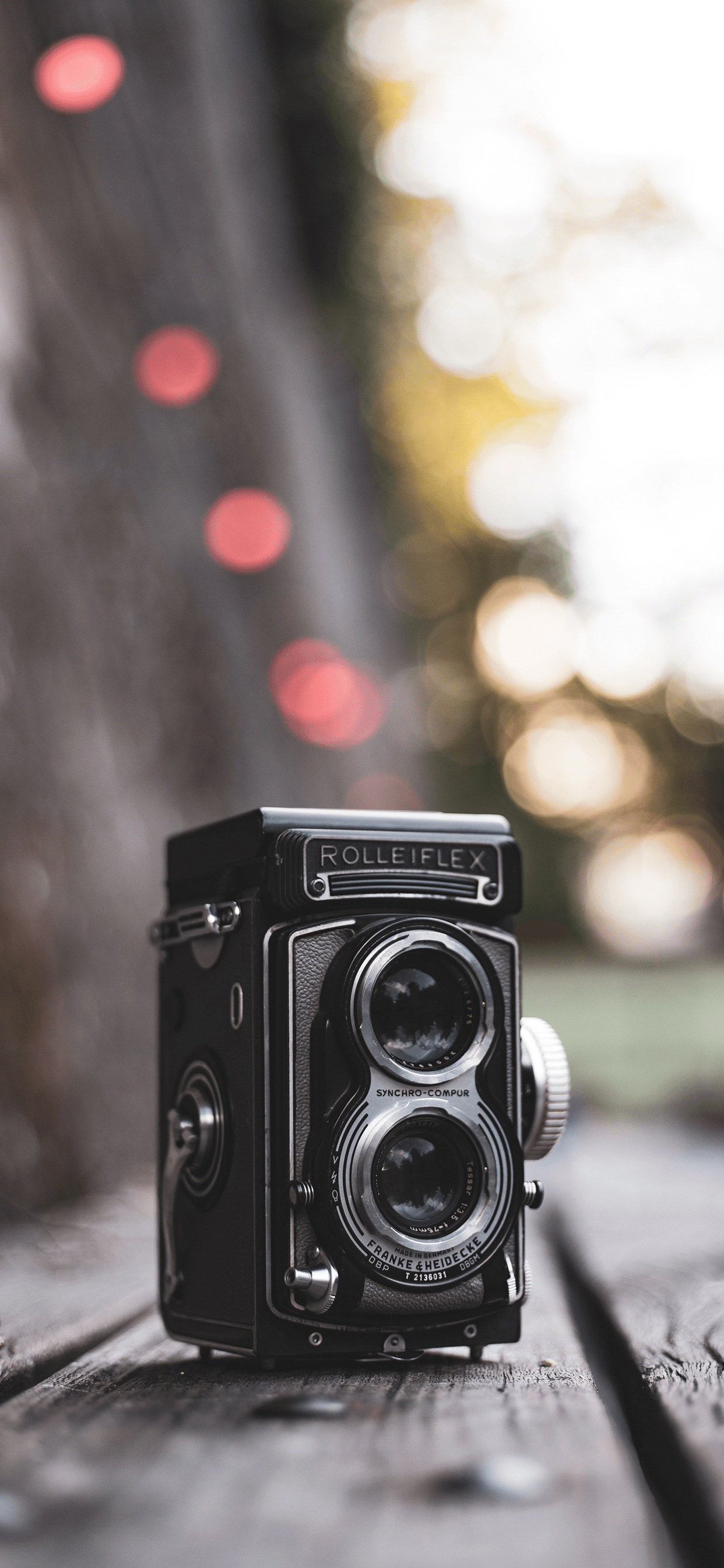 Camera Background — A vintage Rolleiflex twin-lens camera rests on weathered wood with warm bokeh lights glowing softly in the background.