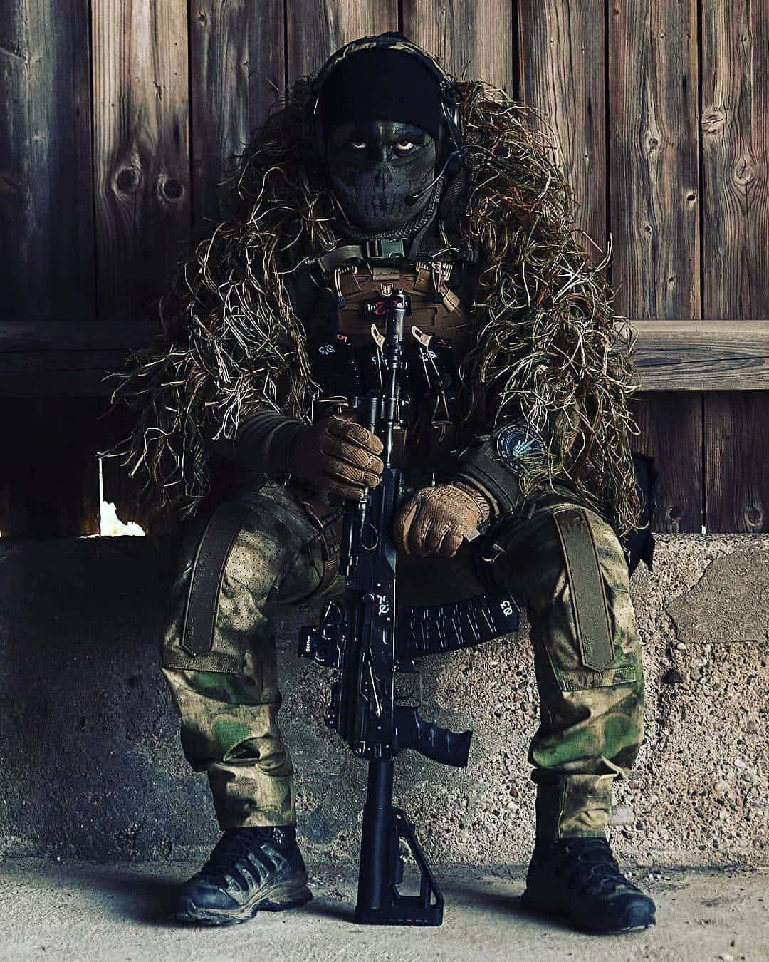 Camouflaged Sniper Sitting With Rifle Wallpaper