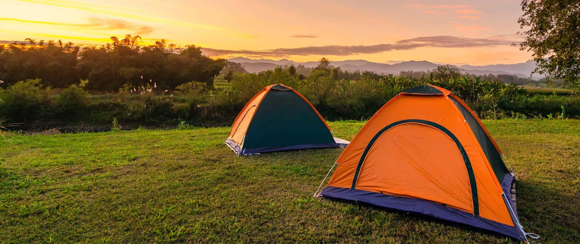 Two Tents Set Up In The Grass At Sunset