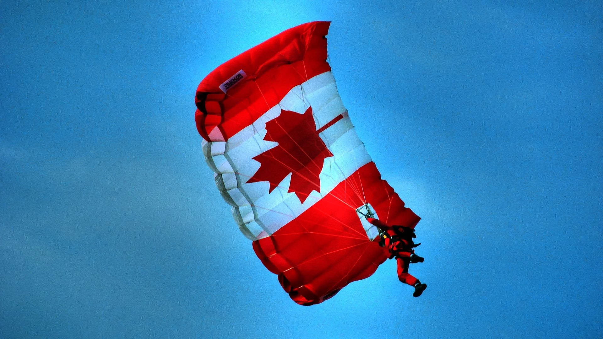 Majestic Shot of Canada Flag Floating on a Parachute Against the Blue Sky Wallpaper