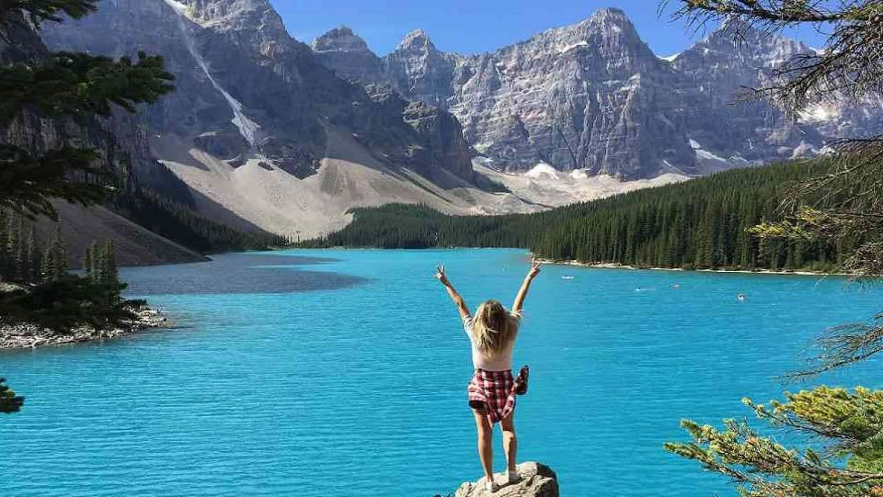 A Woman Standing On A Rock Overlooking A Blue Lake