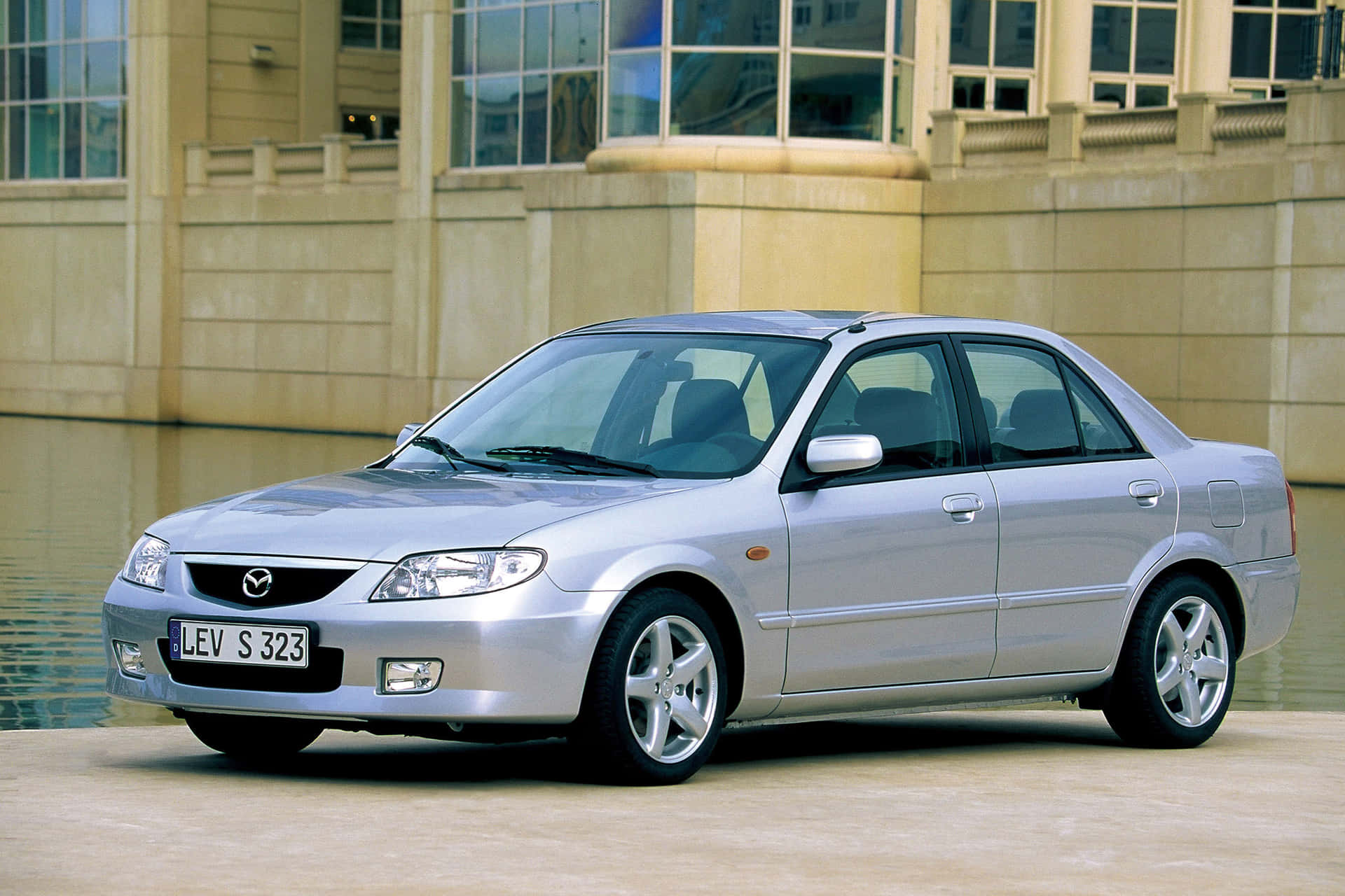 Caption: Sleek And Stylish Mazda 323 In The Spotlight Wallpaper