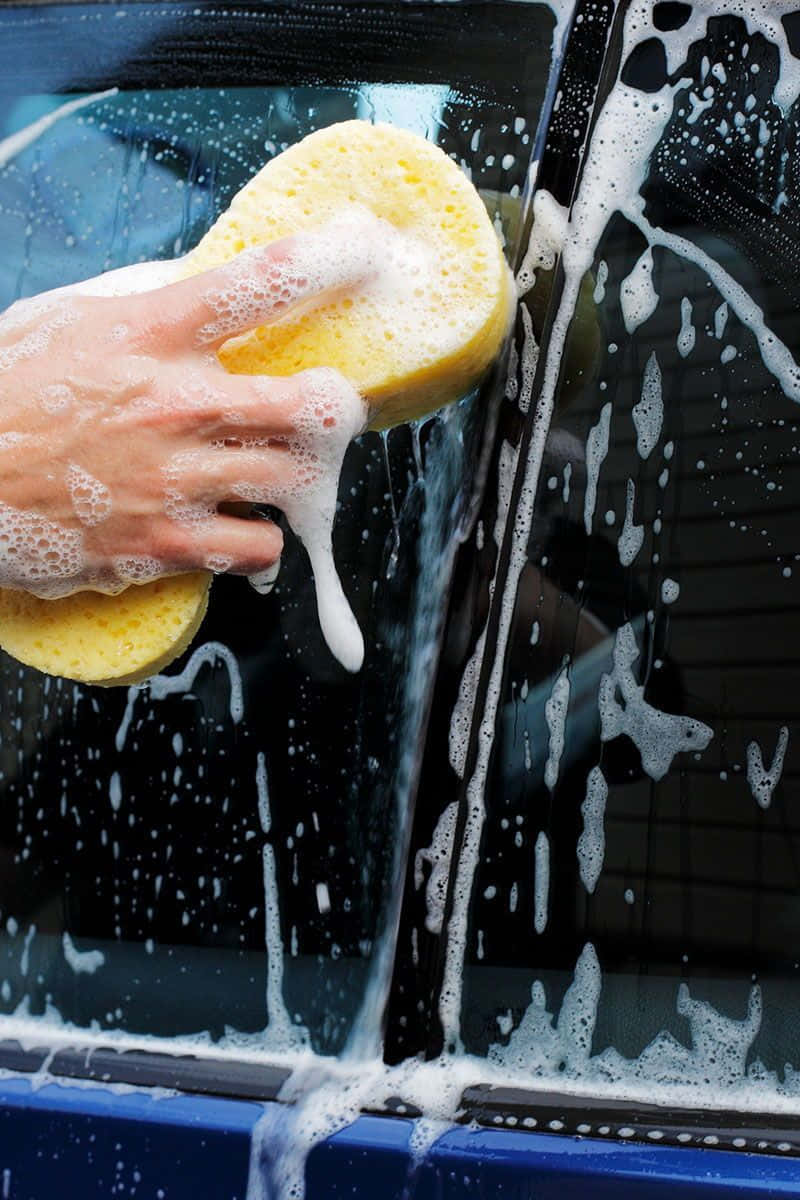 A Person Washing A Car With A Sponge