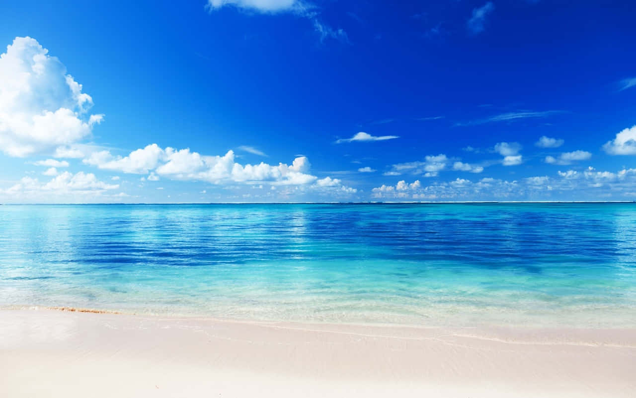 En strand med blåt vand og skyer i baggrunden Wallpaper