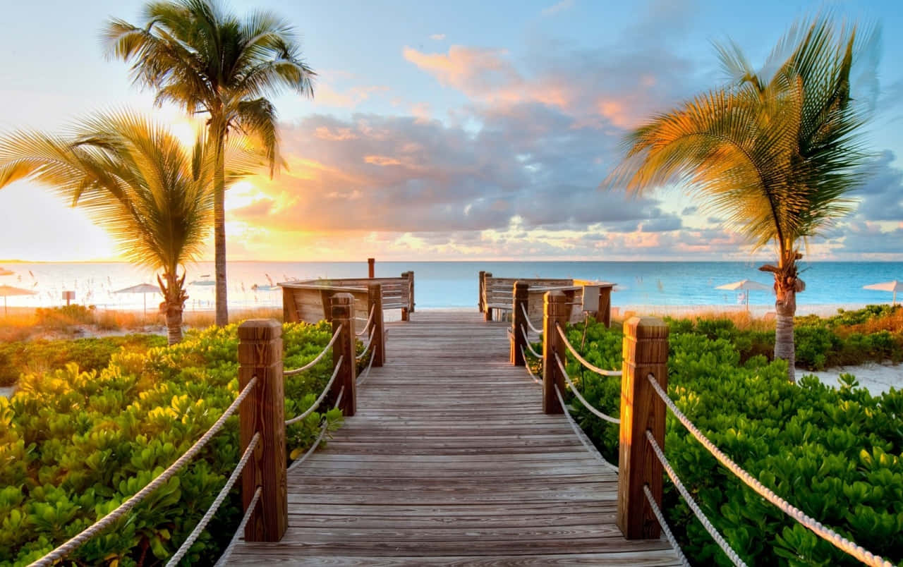 A Wooden Walkway Leading To The Beach At Sunset Wallpaper