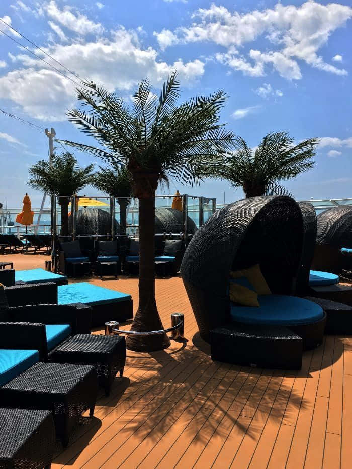 A Deck With Lounge Chairs And Palm Trees On A Cruise Ship
