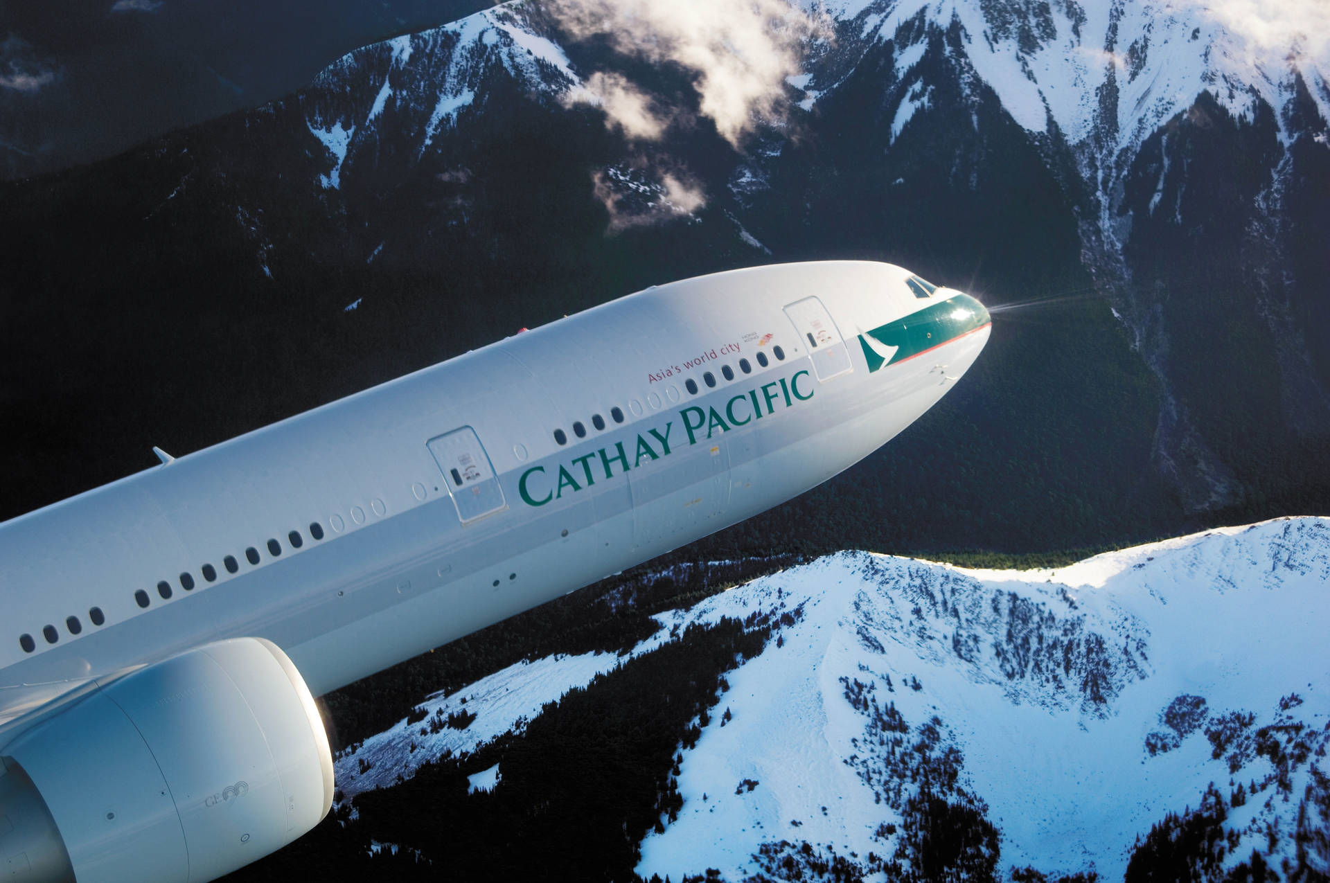Caption: Cathay Pacific Jet over Snow-Capped Mountains Wallpaper